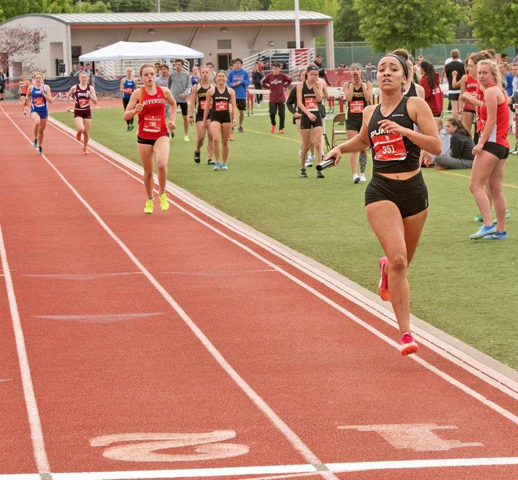 Athlete prepares for pole vault on a track with others watching.