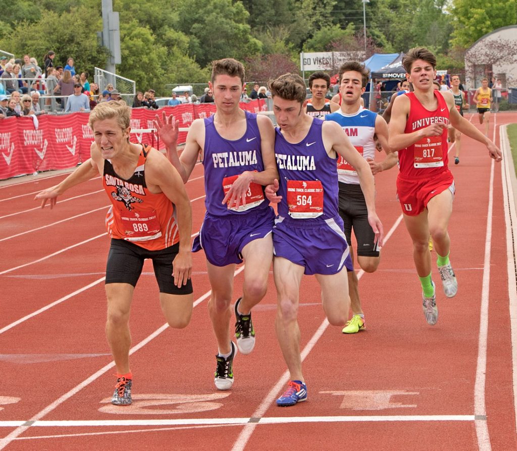 Athlete prepares for pole vault on a track with others watching.