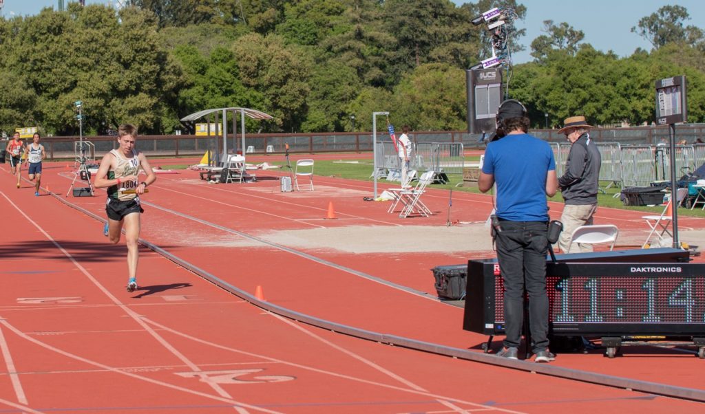 Athlete prepares for pole vault on a track with others watching.