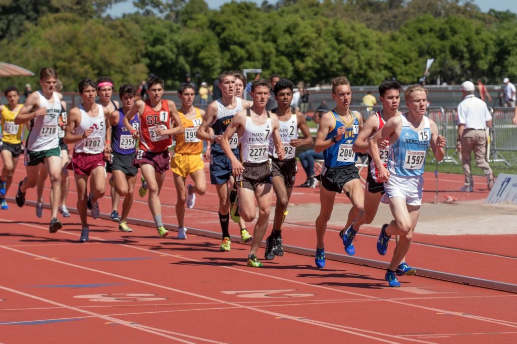 Athlete prepares for pole vault on a track with others watching.