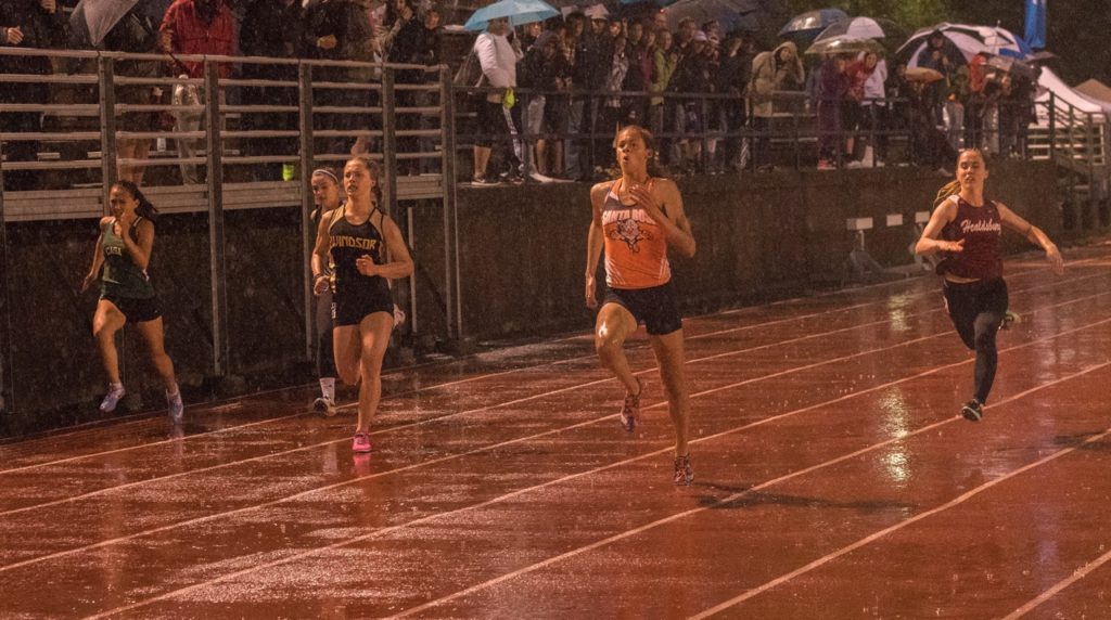 Athlete prepares for pole vault on a track with others watching.