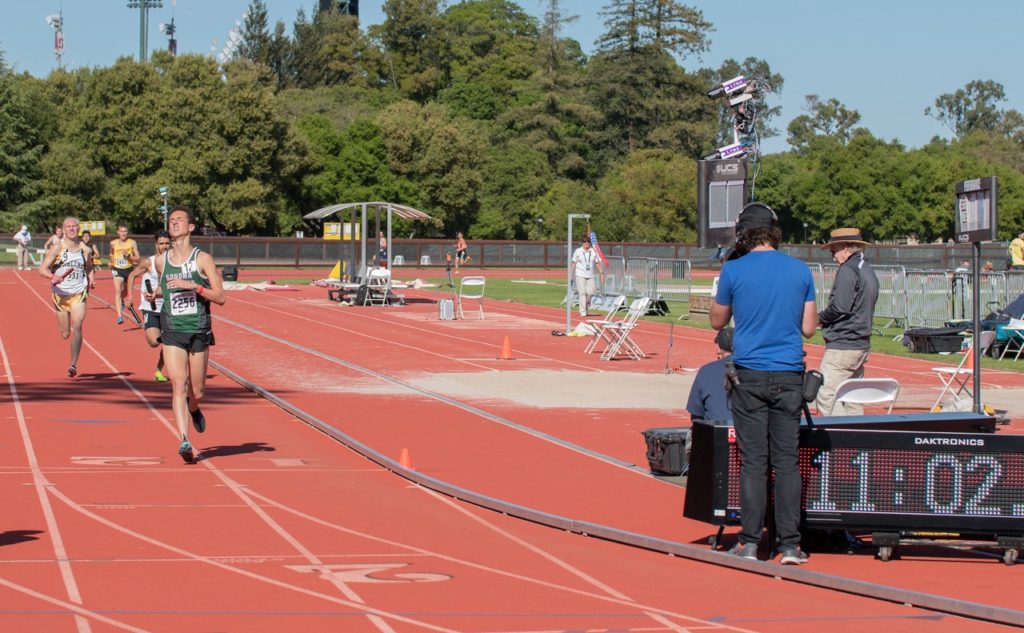 Athlete prepares for pole vault on a track with others watching.