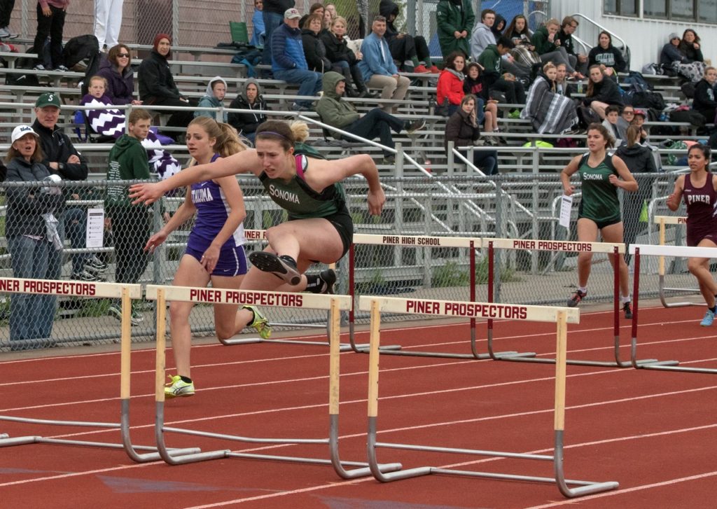 Athlete prepares for pole vault on a track with others watching.