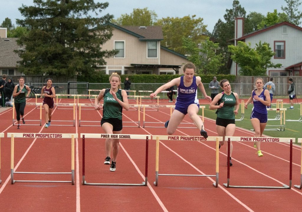 Athlete prepares for pole vault on a track with others watching.