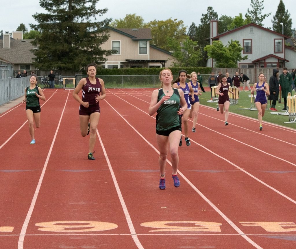 Athlete prepares for pole vault on a track with others watching.