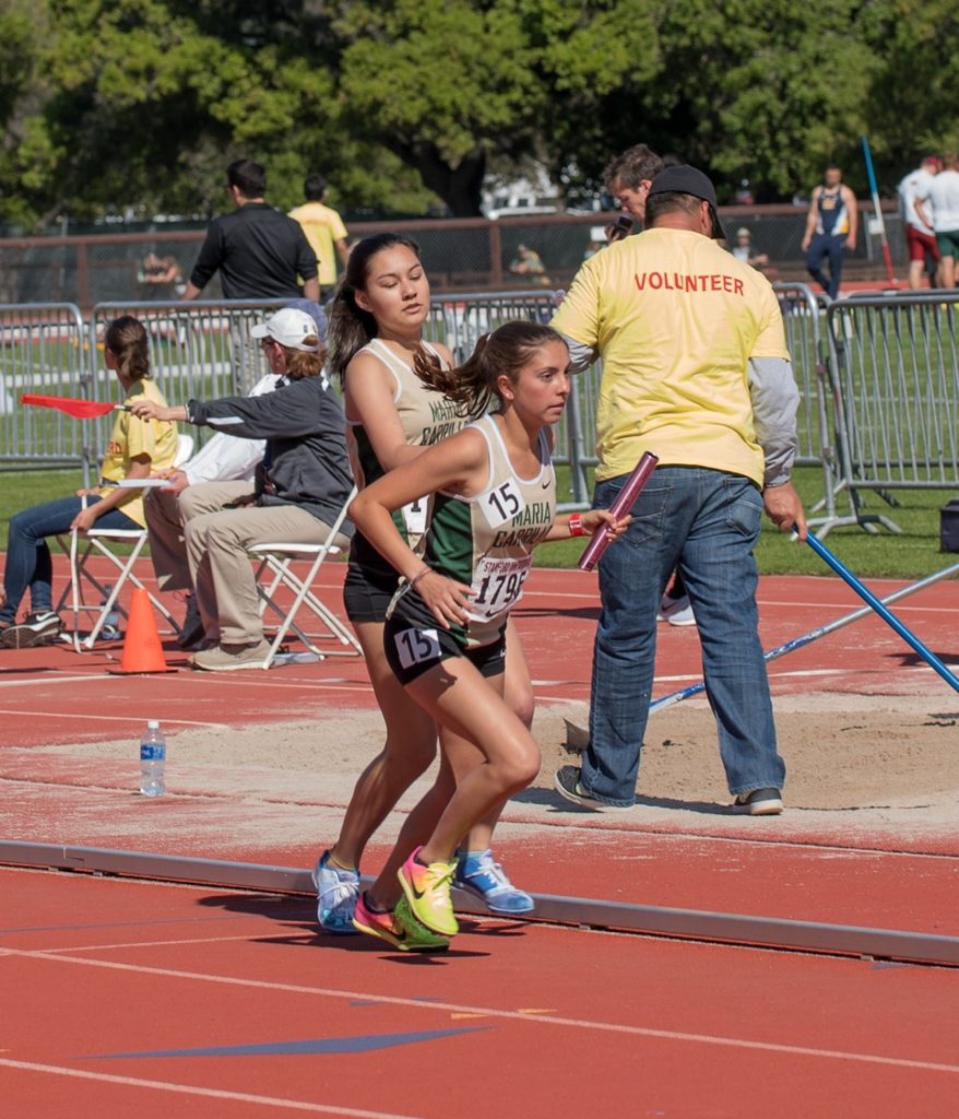 Athlete prepares for pole vault on a track with others watching.