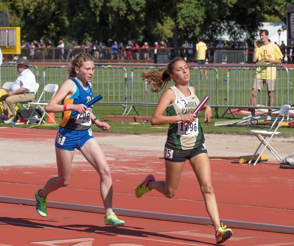 Athlete prepares for pole vault on a track with others watching.