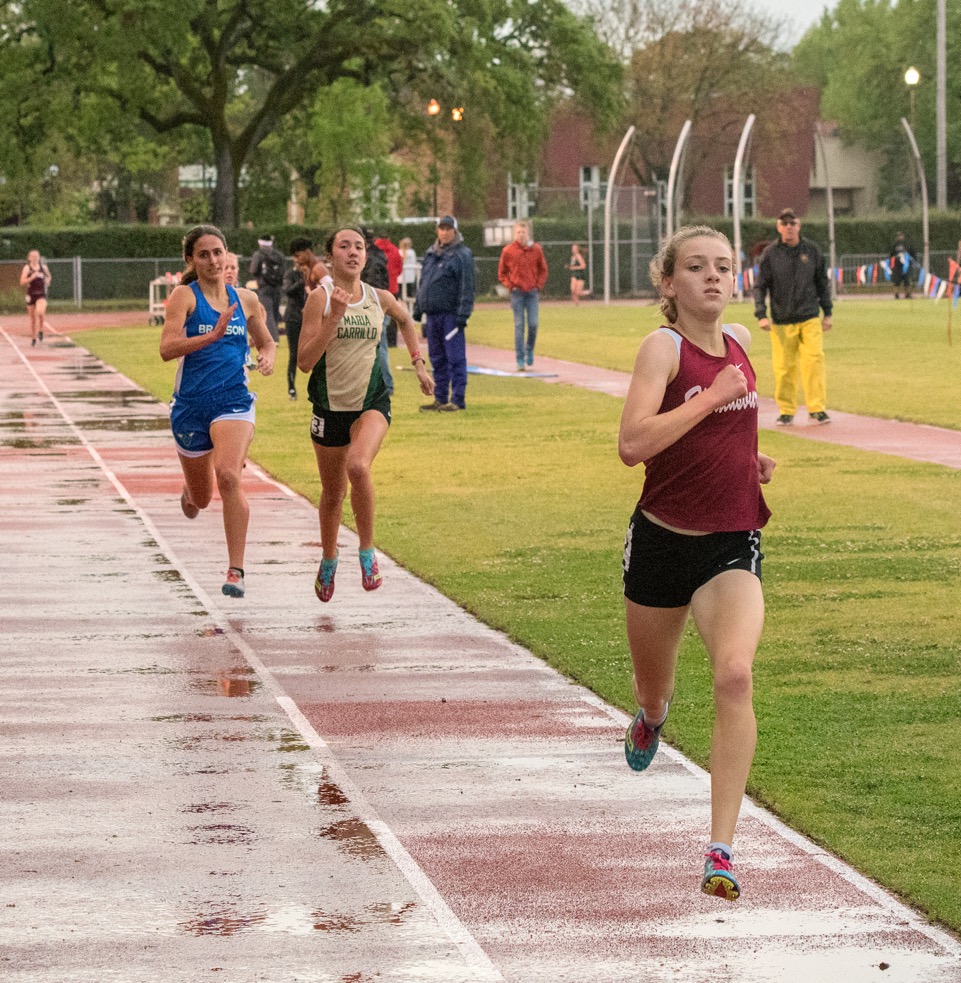 Athlete prepares for pole vault on a track with others watching.