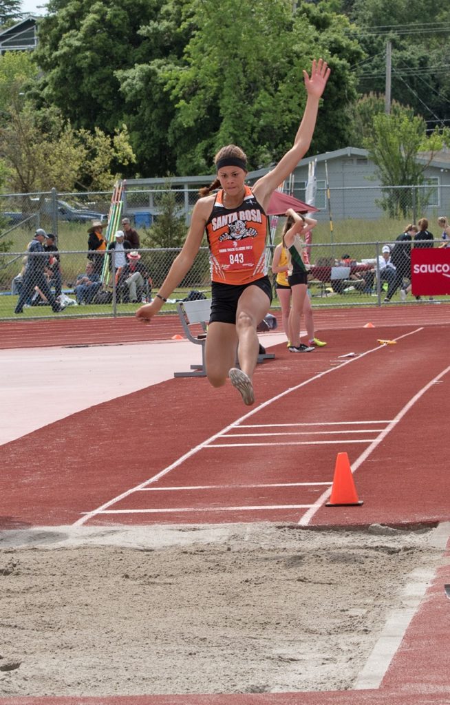 Athlete prepares for pole vault on a track with others watching.
