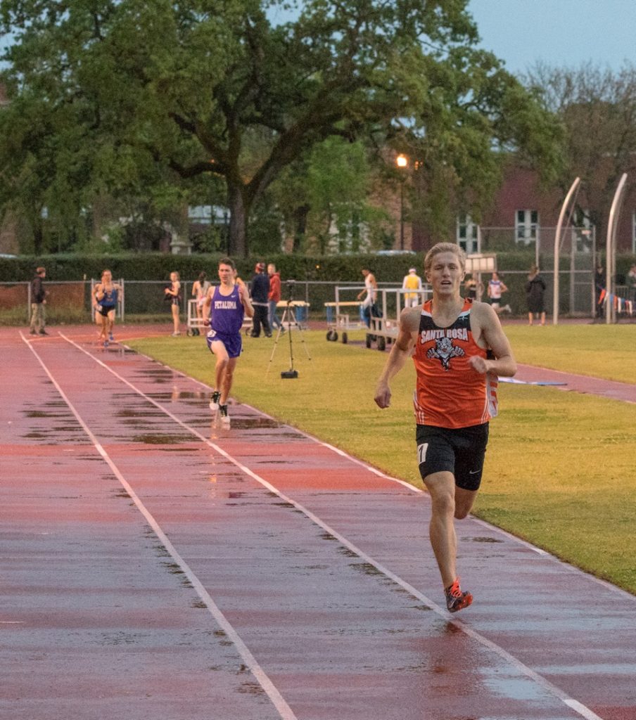Athlete prepares for pole vault on a track with others watching.