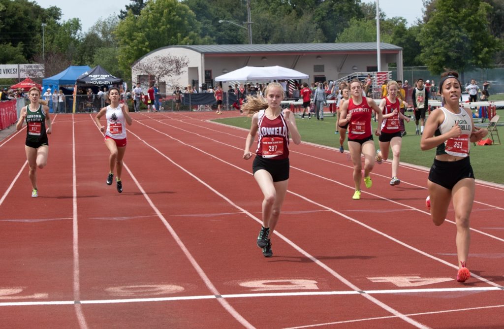 Athlete prepares for pole vault on a track with others watching.