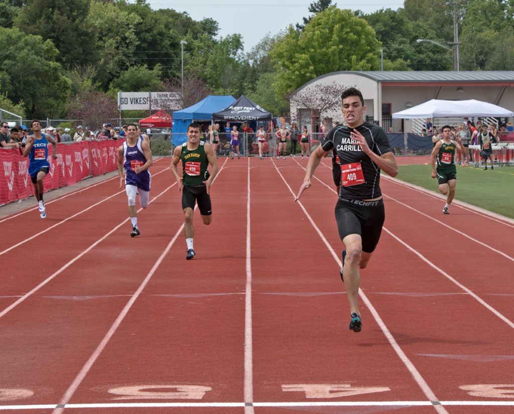 Athlete prepares for pole vault on a track with others watching.