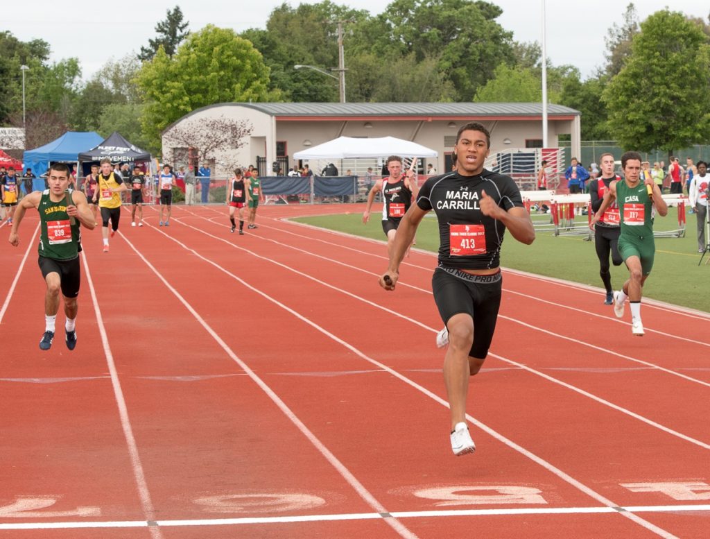 Athlete prepares for pole vault on a track with others watching.