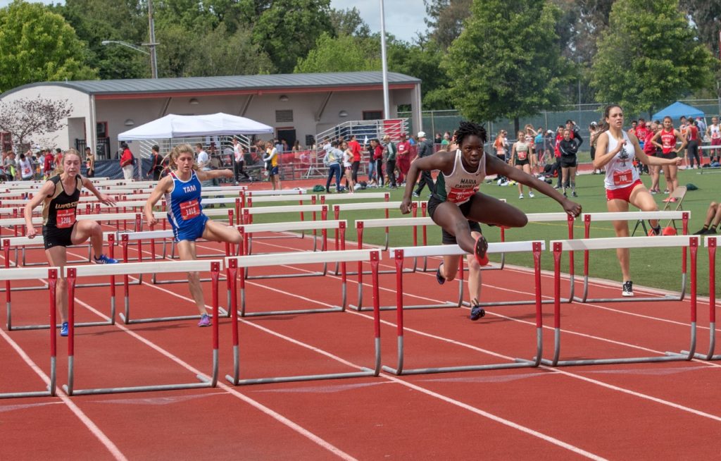 Athlete prepares for pole vault on a track with others watching.