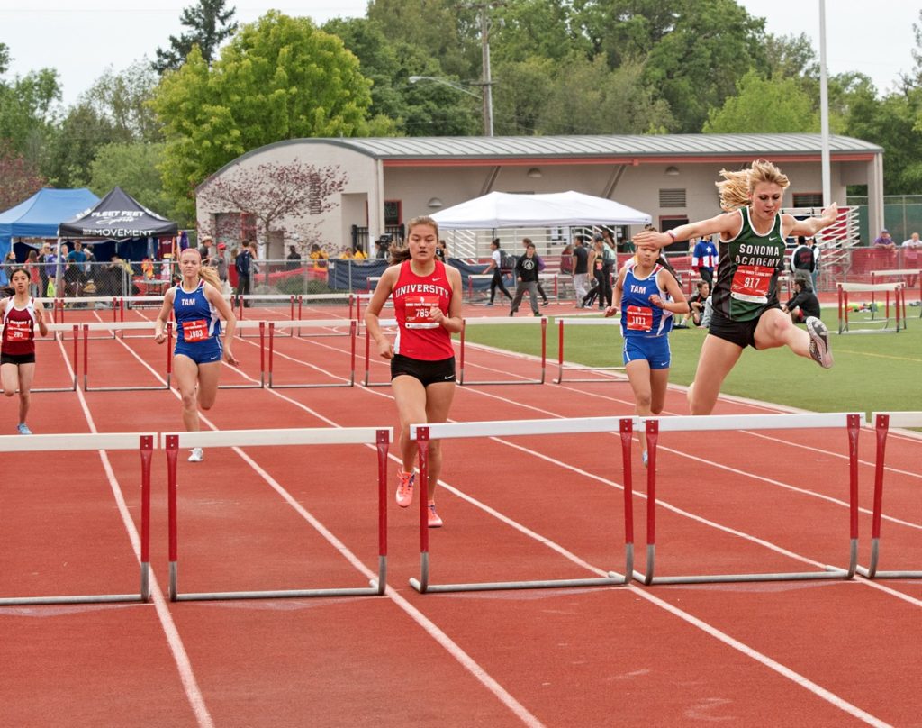 Athlete prepares for pole vault on a track with others watching.