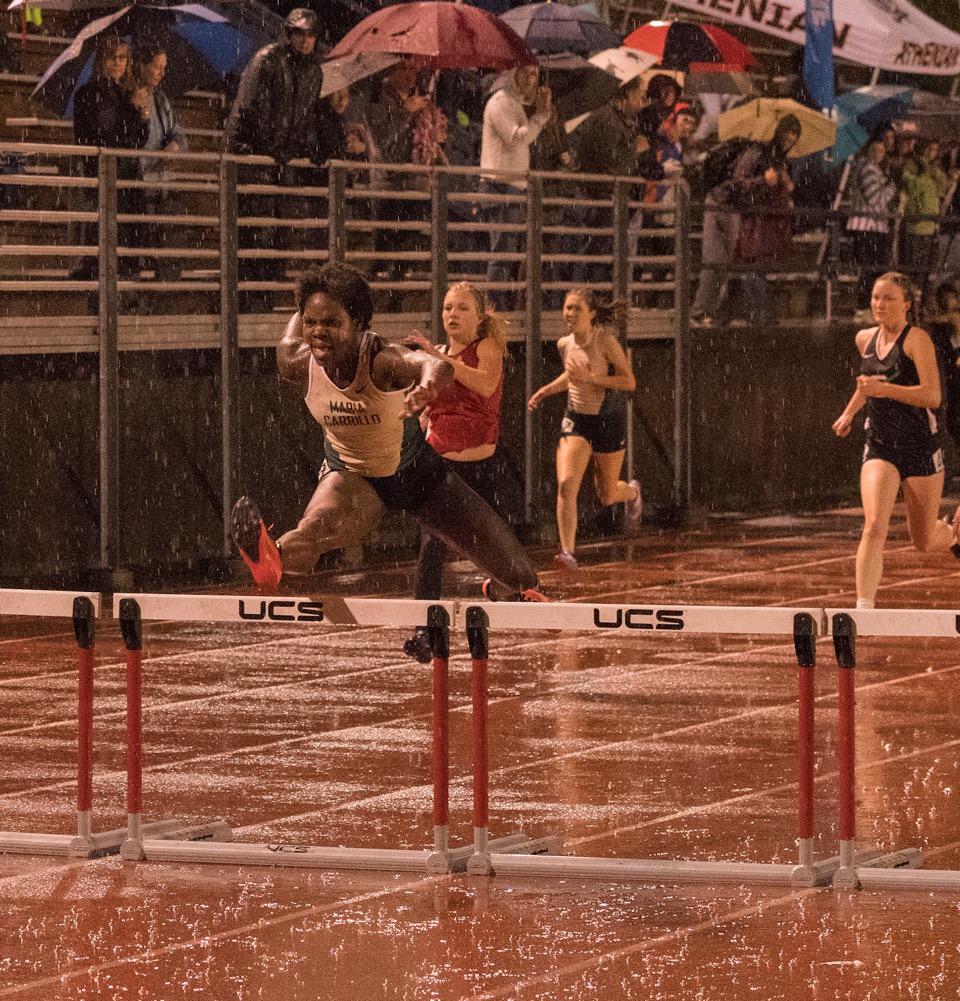 Athlete prepares for pole vault on a track with others watching.