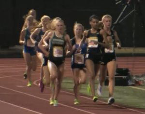 Athlete prepares for pole vault on a track with others watching.