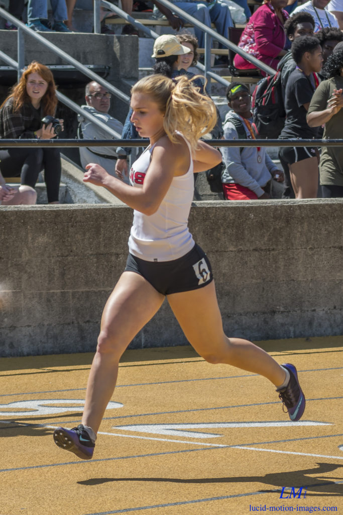 Athlete prepares for pole vault on a track with others watching.