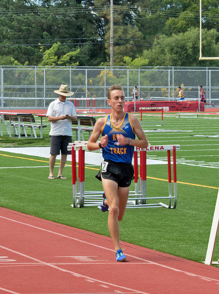 Athlete prepares for pole vault on a track with others watching.