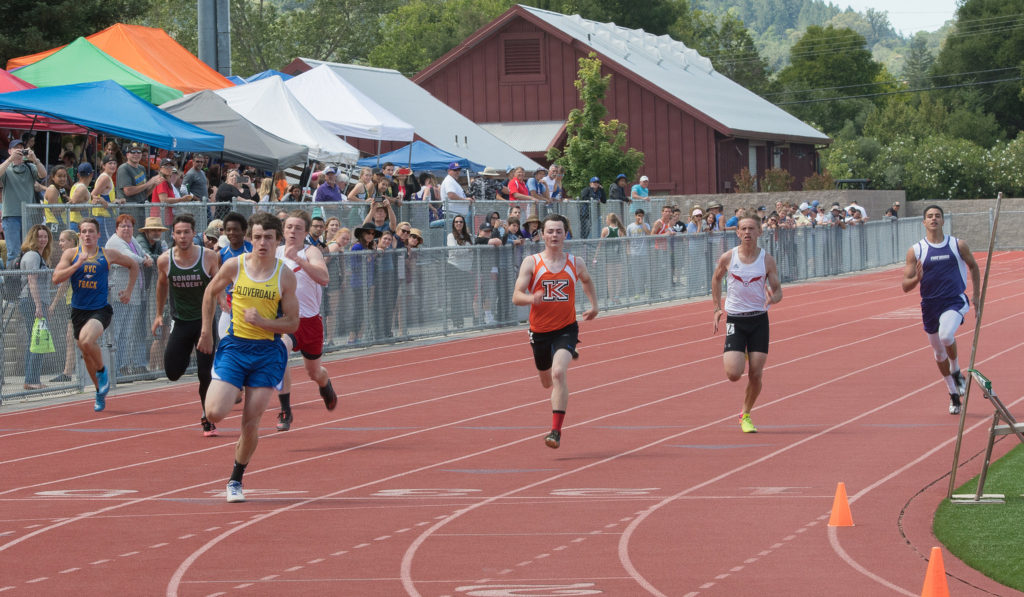 Athlete prepares for pole vault on a track with others watching.