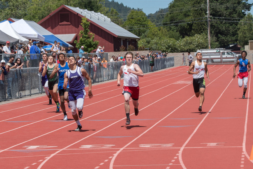 Athlete prepares for pole vault on a track with others watching.