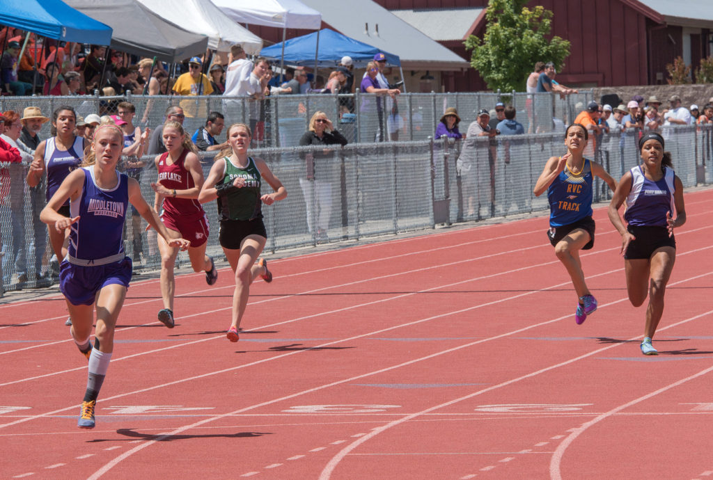 Athlete prepares for pole vault on a track with others watching.