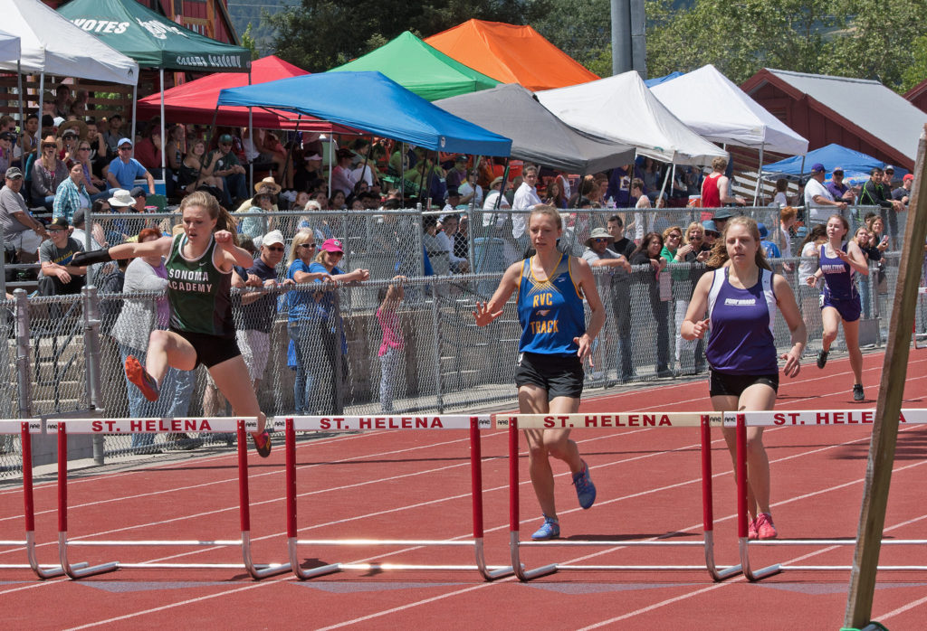 Athlete prepares for pole vault on a track with others watching.