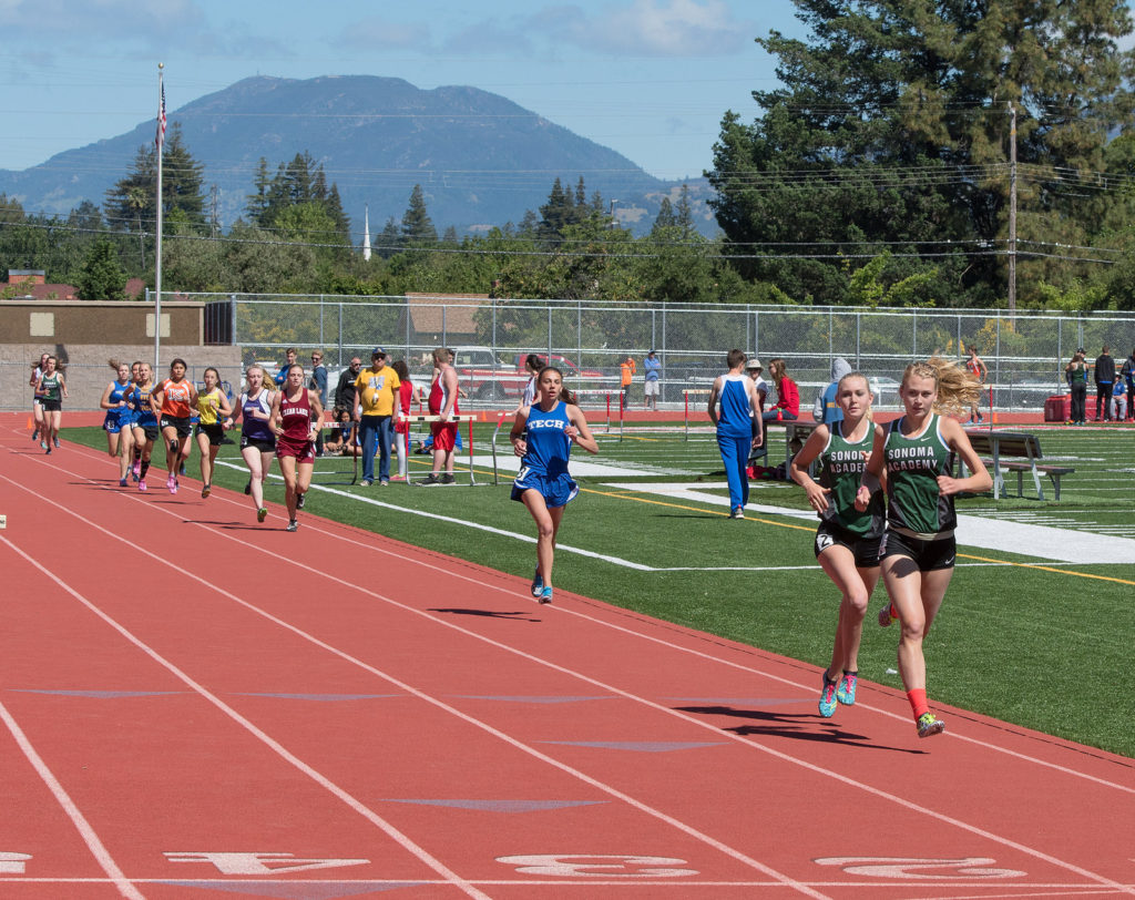 Athlete prepares for pole vault on a track with others watching.
