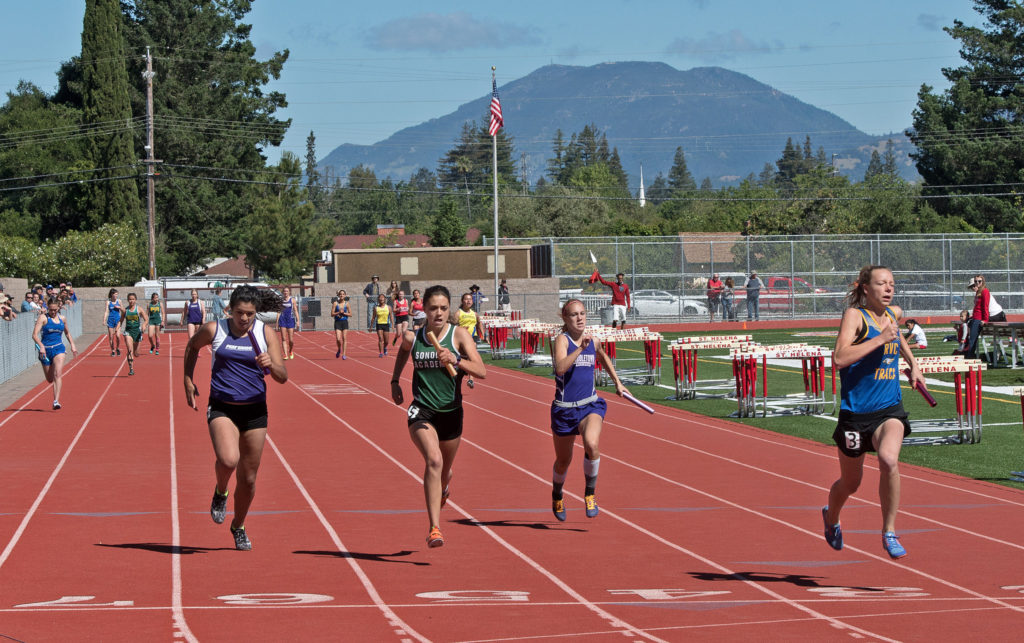 Athlete prepares for pole vault on a track with others watching.
