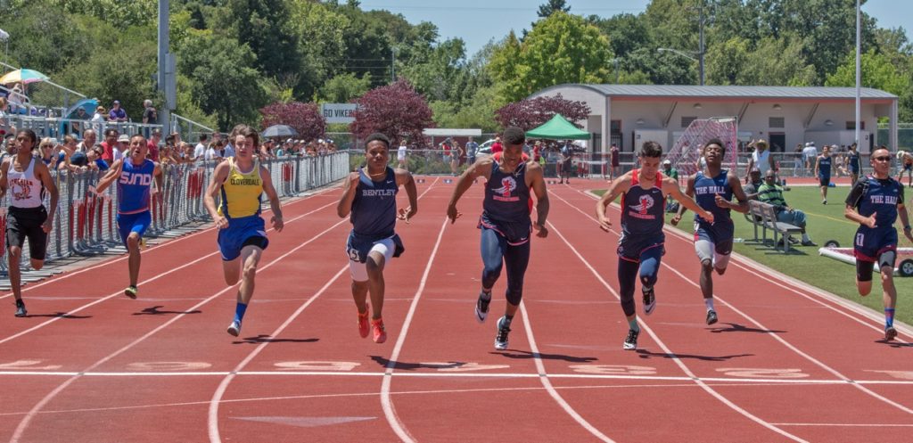 Athlete prepares for pole vault on a track with others watching.