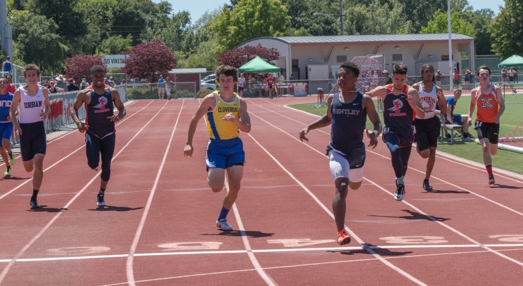 Athlete prepares for pole vault on a track with others watching.