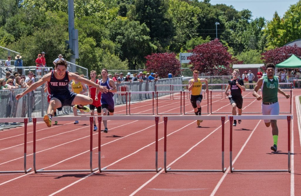 Athlete prepares for pole vault on a track with others watching.