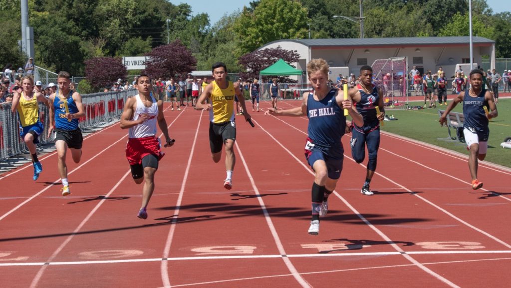 Athlete prepares for pole vault on a track with others watching.