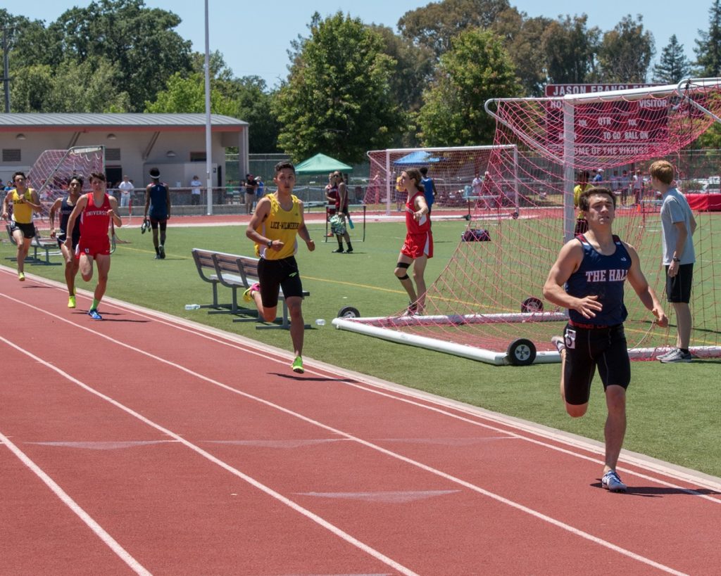 Athlete prepares for pole vault on a track with others watching.