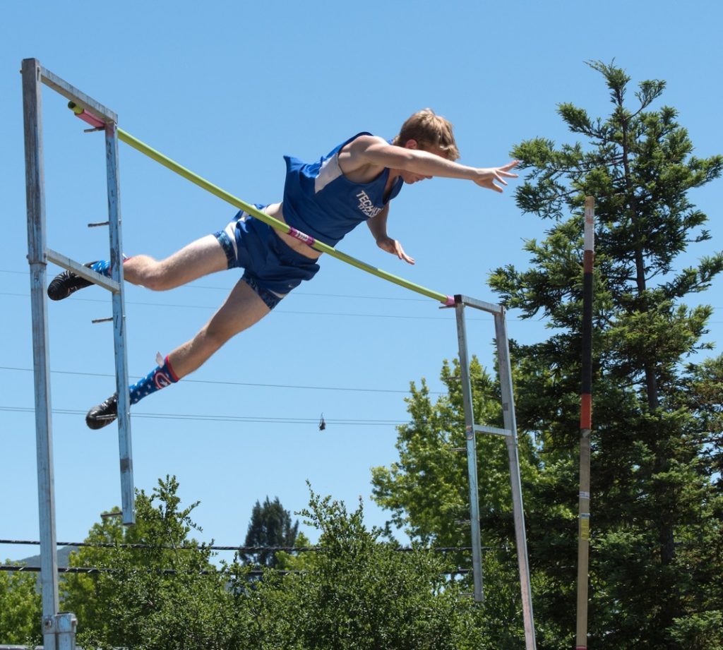 Athlete prepares for pole vault on a track with others watching.