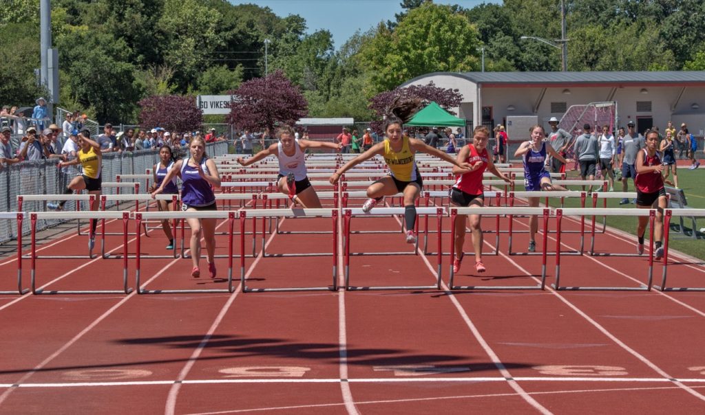 Athlete prepares for pole vault on a track with others watching.
