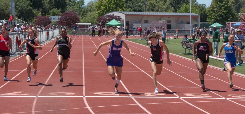 Athlete prepares for pole vault on a track with others watching.