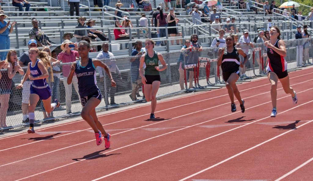 Athlete prepares for pole vault on a track with others watching.