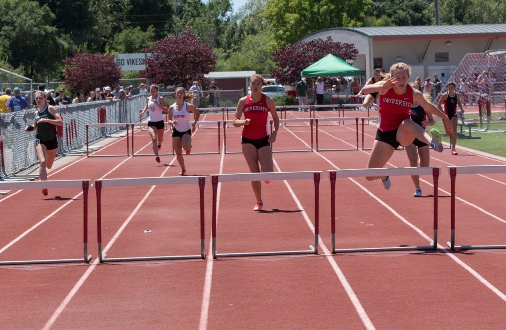 Athlete prepares for pole vault on a track with others watching.