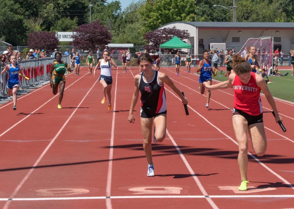 Athlete prepares for pole vault on a track with others watching.