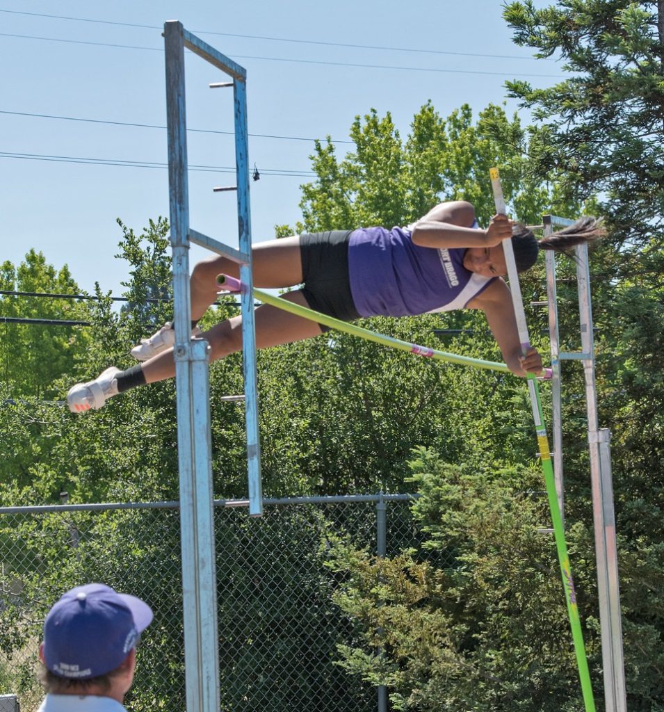 Athlete prepares for pole vault on a track with others watching.