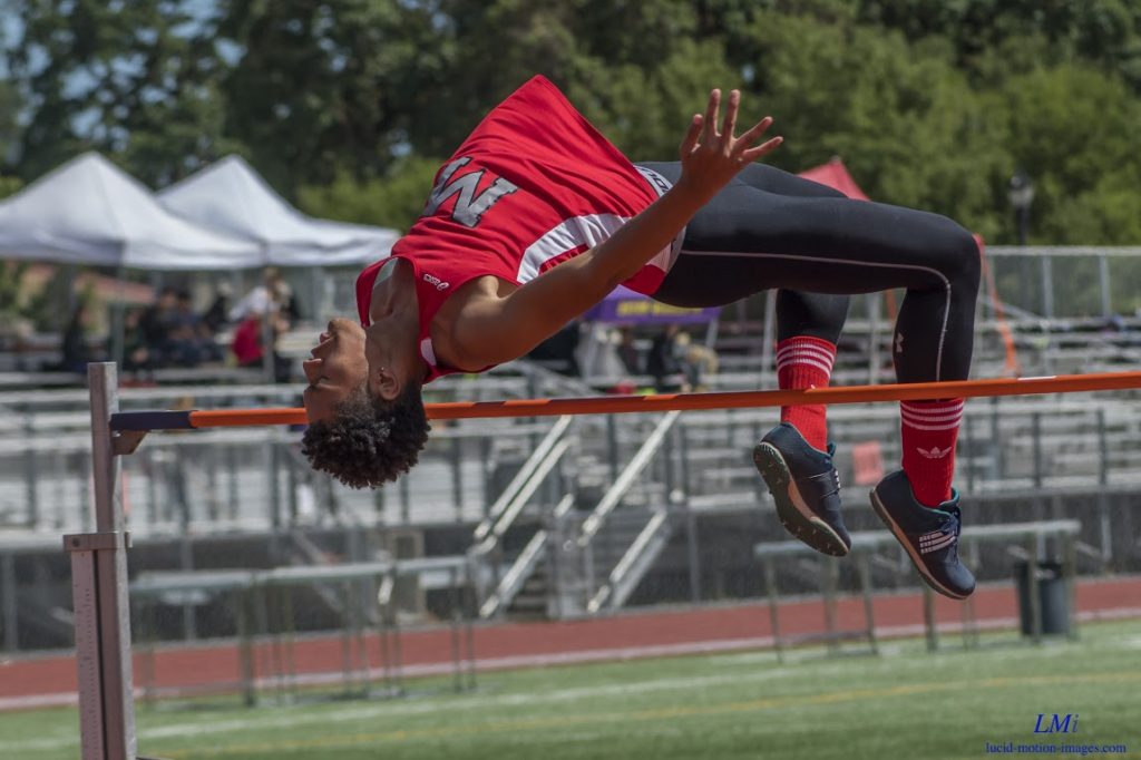 Athlete prepares for pole vault on a track with others watching.