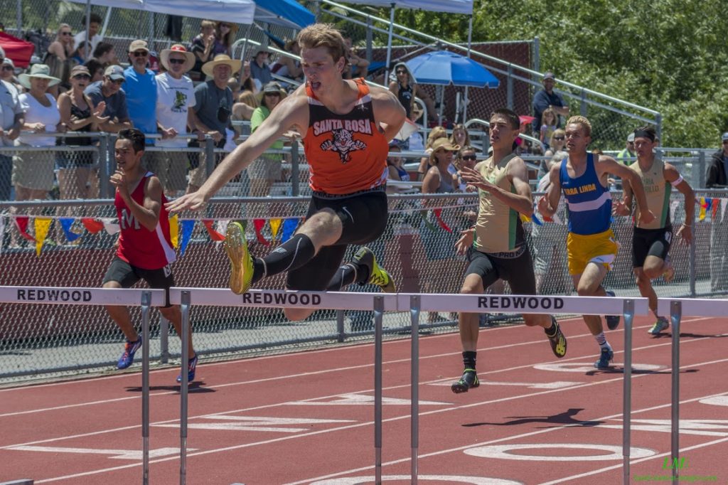 Athlete prepares for pole vault on a track with others watching.