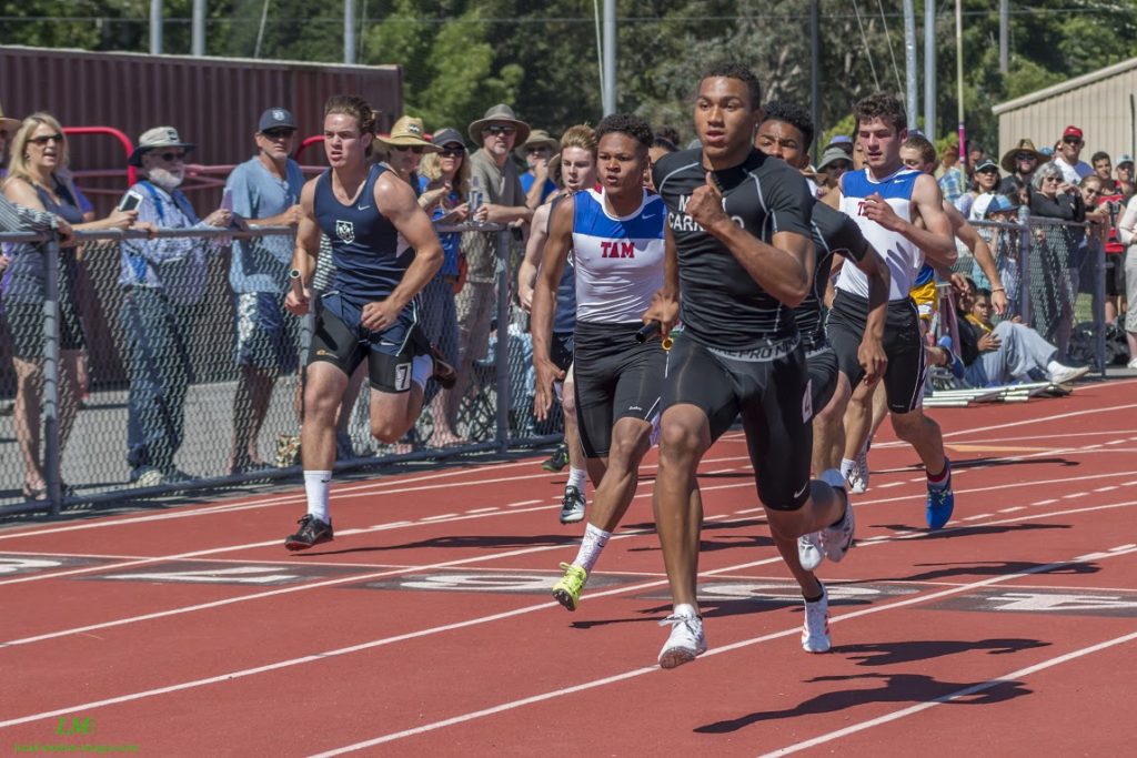 Athlete prepares for pole vault on a track with others watching.