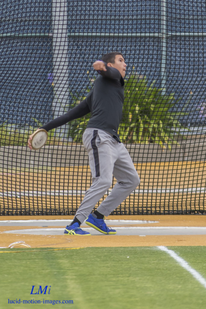 Athlete prepares for pole vault on a track with others watching.