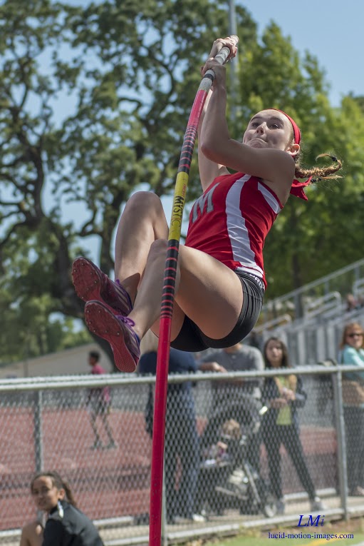 Athlete prepares for pole vault on a track with others watching.