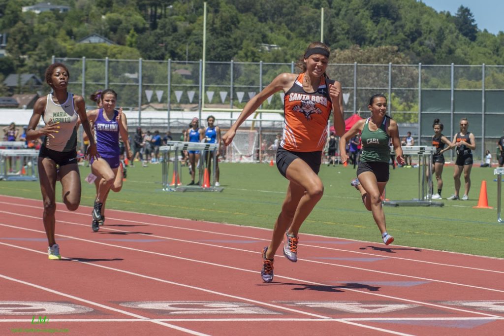 Athlete prepares for pole vault on a track with others watching.