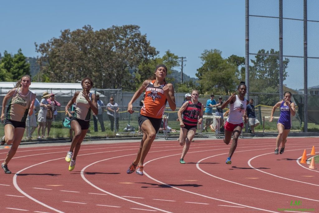 Athlete prepares for pole vault on a track with others watching.
