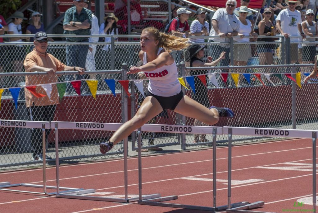 Athlete prepares for pole vault on a track with others watching.