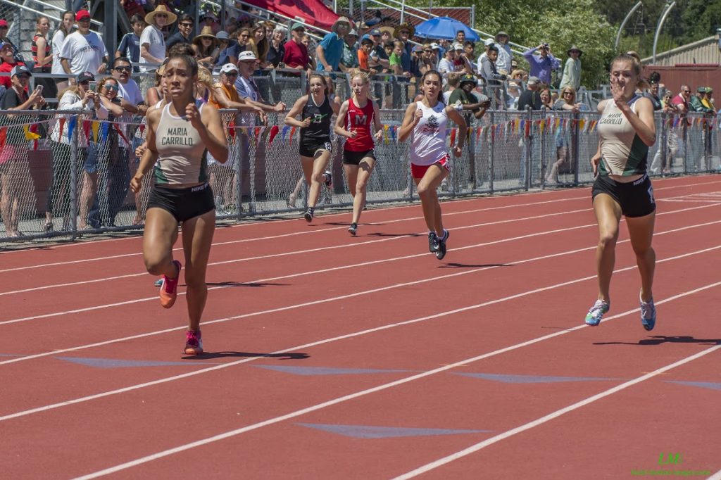 Athlete prepares for pole vault on a track with others watching.